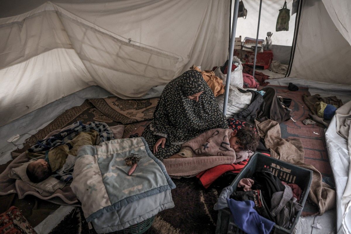 مرأة فلسطينية وأطفالها يجلسون في مأواهم خلال أول هطول للأمطار الشتوية على مخيم للنازحين في مدينة غزة (أ ف ب)